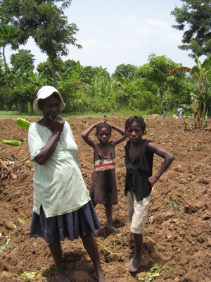 A Haitian woman and two children stand on freshly turned soil