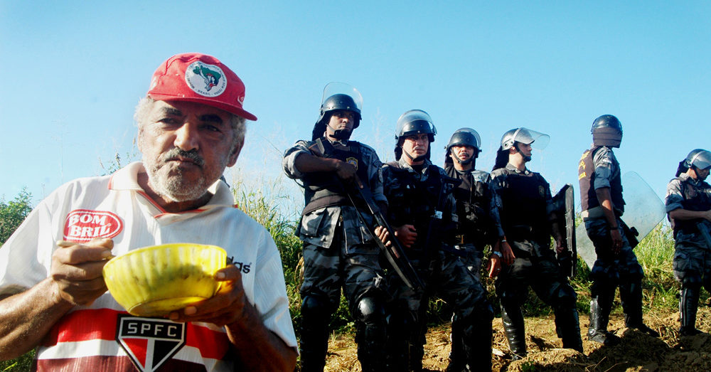 Land Grabs: Member of MST with military guards behind, Brazil.