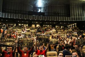 an auditorium full of people holding signs with text "diretas ja!"